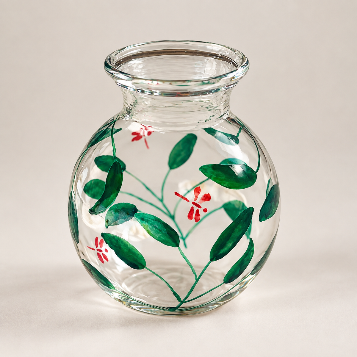 A clear glass vase with a rounded body and short flared neck, decorated with hand-painted green leaves and small red flowers. Alara London