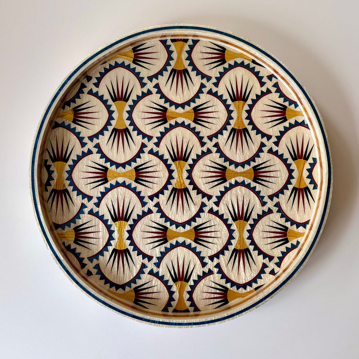 A decorative mother of pearl inlay tray hand made in Egypt with a hand-painted  geometric pattern in cream, navy blue, gold and burgundy on a white background. Alara London 