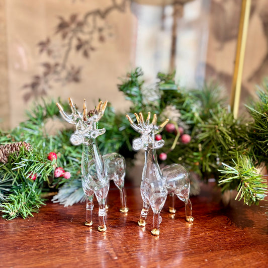 Clear glass deer figurines with gold accents on a wooden surface with Christmas decorations in the background.
