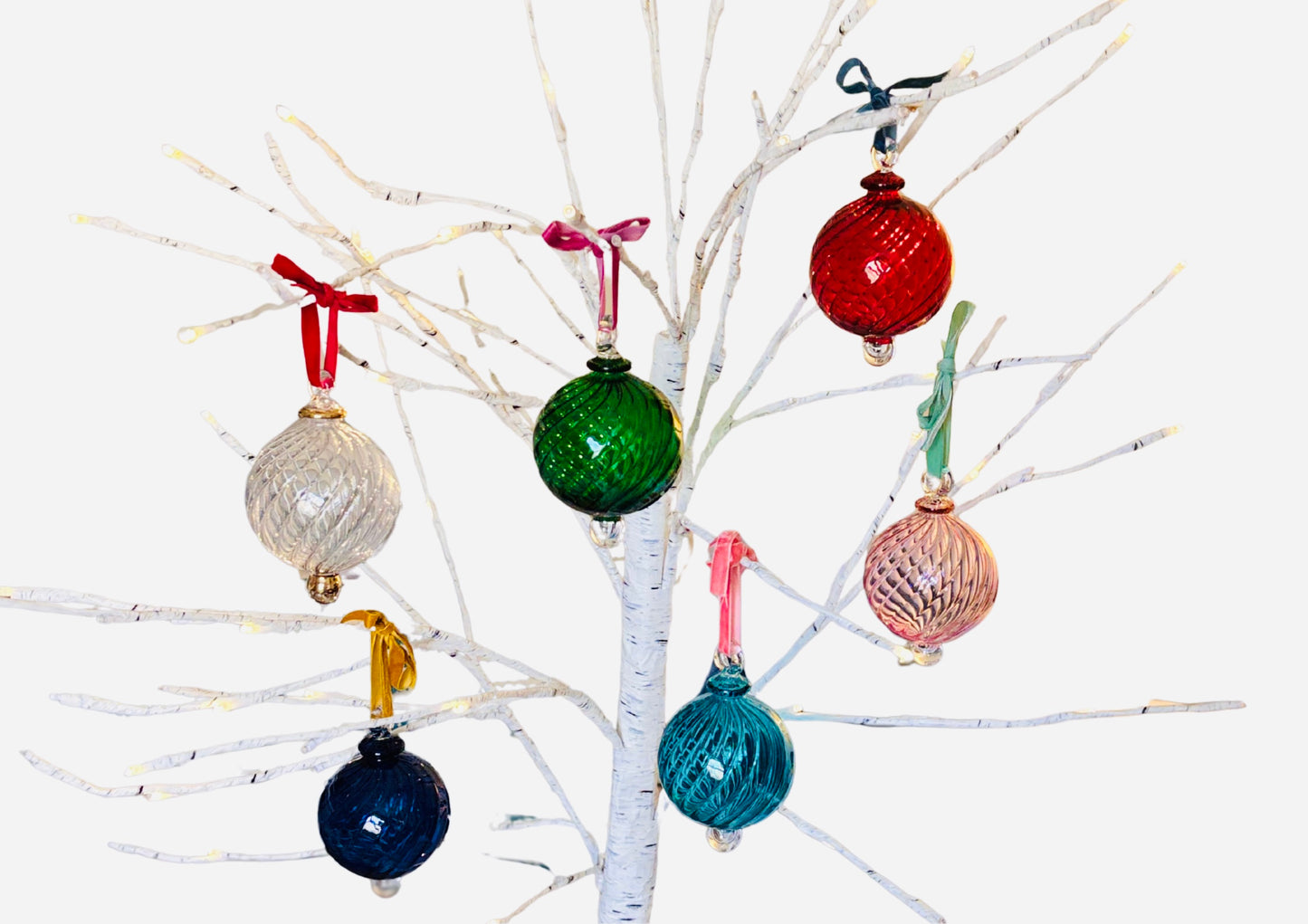 Colorful hand blown glass Christmas baubles hanging on a branch against a white background